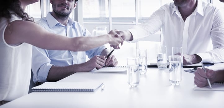 Business partners shaking hands at conference table in office
