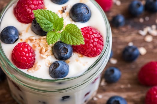 Serving of Yogurt with Whole Fresh Blueberries, Raspberries and Oatmeal on Old Rustic Wooden Table. Closeup Detail.