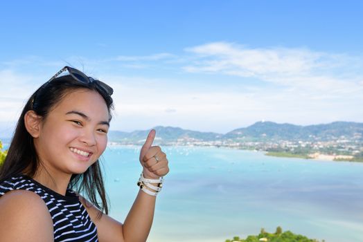 Women tourist smiling happy along with thumb raised expresses admiration for beautiful landscape of the sea and island on Khao-Khad mountain high viewpoint in Phuket Province, Thailand