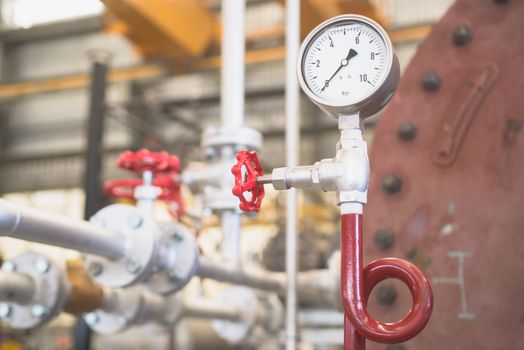 Pressure gauge in industrial environment. Shallow depth of field with the gauge and valve in focus.