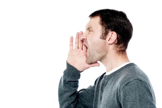 Side pose of man shouting, hands near his mouth.