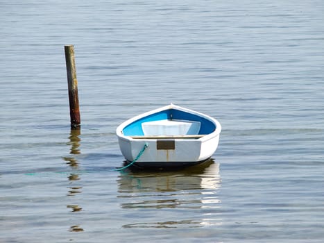 Moored small dingy rowing boat on still calm water  