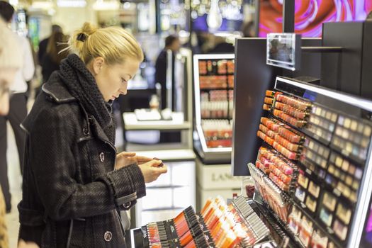 Beautiful blond lady testing  and buying cosmetics in a beauty store.