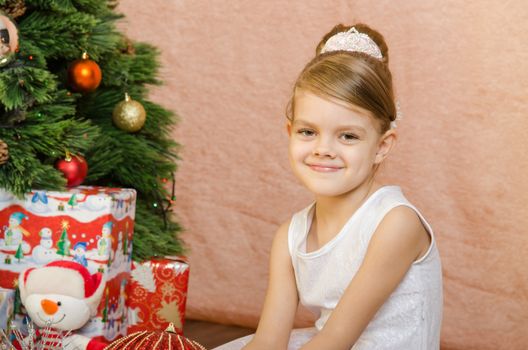 Five-year girl in a New Year's dress sitting on a mat at the Christmas tree