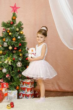 Five-year girl in a New Year's dress standing on a mat at the Christmas tree