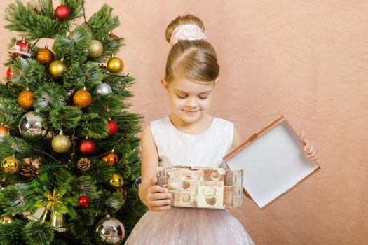 Five-year girl in a New Year's dress sitting on a mat at the Christmas tree