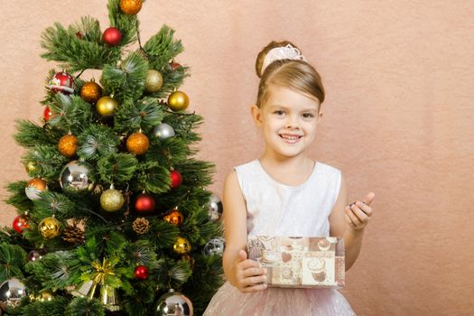 Five-year girl in a New Year's dress sitting on a mat at the Christmas tree