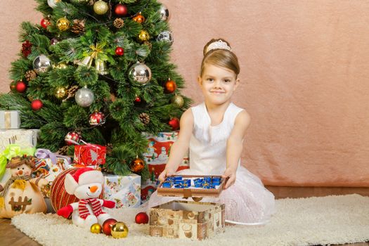 Five-year girl in a New Year's dress sitting on a mat at the Christmas tree