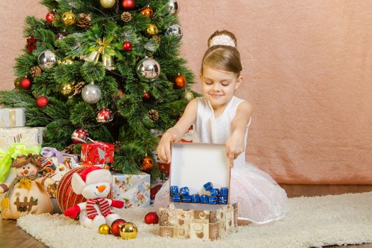 Five-year girl in a New Year's dress sitting on a mat at the Christmas tree