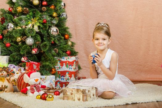 Five-year girl in a New Year's dress sitting on a mat at the Christmas tree