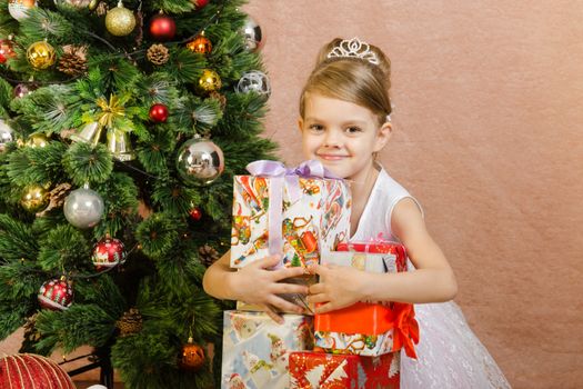 Five-year girl in a New Year's dress sitting on a mat at the Christmas tree