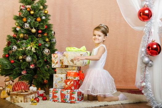 Five-year girl in a New Year's dress sitting on a mat at the Christmas tree