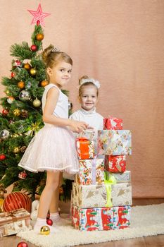 Five-year and three-year girl in a New Year's dress sitting on a mat at the Christmas tree