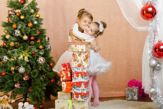 Five-year and three-year girl in a New Year's dress sitting on a mat at the Christmas tree