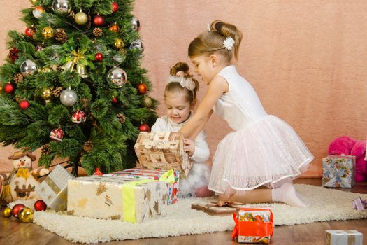 Five-year and three-year girl in a New Year's dress sitting on a mat at the Christmas tree