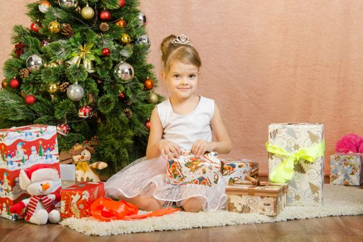 Five-year girl in a New Year's dress sitting on a mat at the Christmas tree