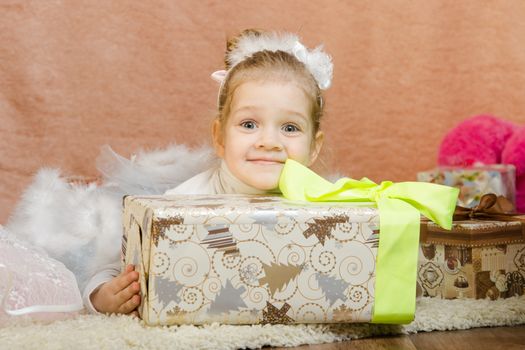 The three-year girl in a New Year's dress sitting on a mat at the Christmas tree