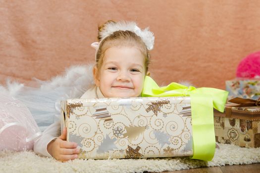 The three-year girl in a New Year's dress sitting on a mat at the Christmas tree