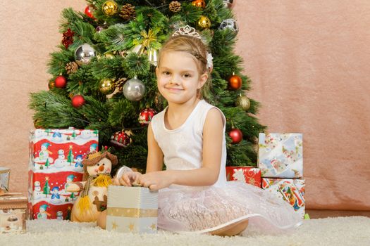 Five-year girl in a New Year's dress sitting on a mat at the Christmas tree
