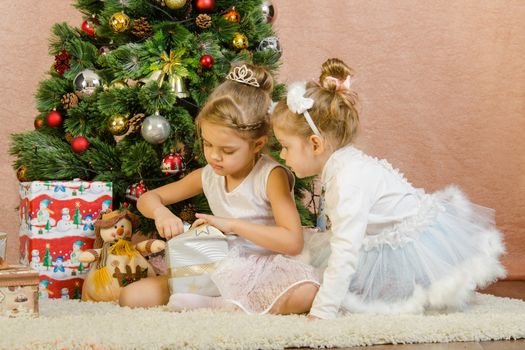 Five-year and three-year girl in a New Year's dress sitting on a mat at the Christmas tree