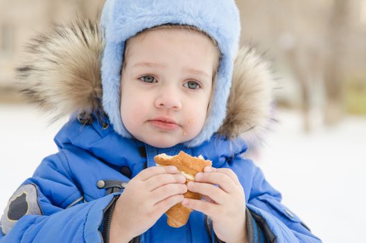 The three-year girl is outside in the winter eating a muffin