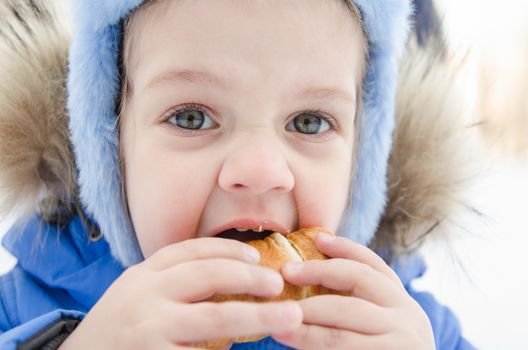 The three-year girl is outside in the winter eating a muffin