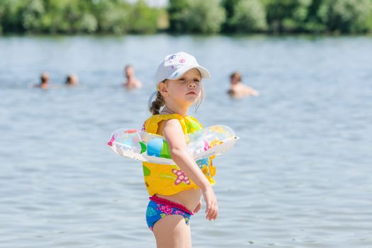 Four-year girl on a river beach wearing wearing the life jackets and circle