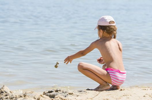 Girl sitting on the river bank and throwing sand in the water