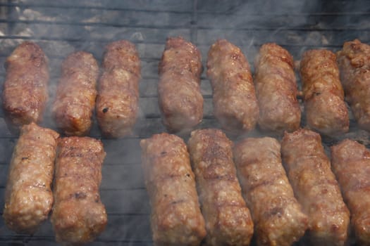 Barbecuing minced meat, traditional Romanian preparation for barbecue, called "mici",  on charcoal fire - closeup image.
