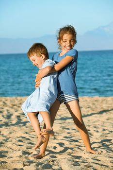 Two kids - seven and three on the beach playing. Sister is lifting and spinning arround her younger brother laughing.