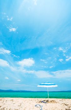 A single umbrella with two pairs of sandals and a scarf underlined on an empty beautiful sunny beach. Vertical composition.