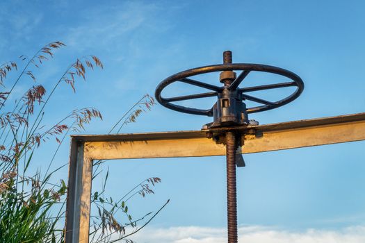 winch of irrigation ditch gate against sky with tall grass