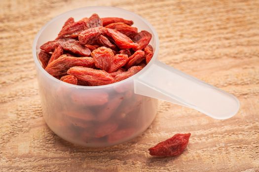 measuring scoop of dried goji berries against cedar wood plank