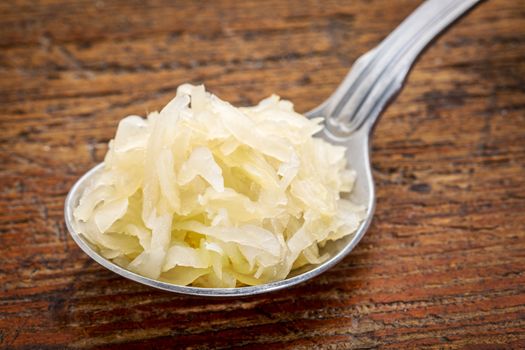 tablespoon of sauerkraut against rustic wooden cutting board - healthy eating concept (probiotic food)