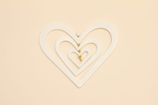 A three layer white heart made of wood hanging on a cream wall centered in the photo