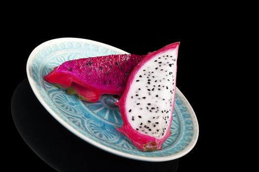 Red and white dragon fruit piece on plate isolated on black background. Tropical fruits, minimal luxurious style.