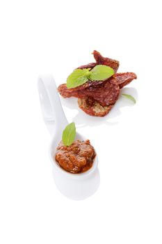 Red pesto and dry tomatoes on spoon with fresh basil leaf isolated on white background. Culinary italian eating, minimal contemporary styles.