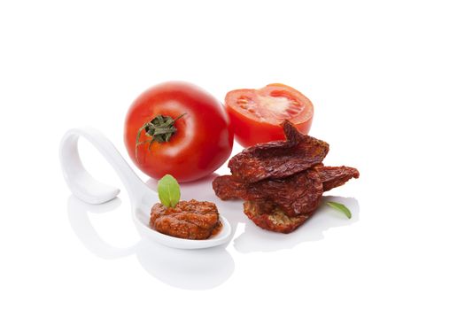 Dried and fresh ripe tomatoes and red pesto on spoon with fresh basil leaf isolated on white background. Culinary eating, minimal contemporary styles.