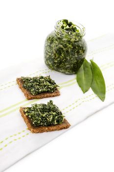 Culinary healthy eating, spring detox. Garlic pesto in glass jar with fresh wild garlic leaves isolated on white background. 