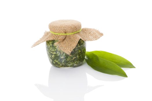 Garlic pesto in glass jar with fresh wild garlic leaves isolated on white background. Culinary healthy eating, spring detox. 