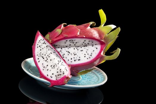 Delicious white dragon fruit on plate isolated on black background. Tropical fruit, luxurious minimal style.