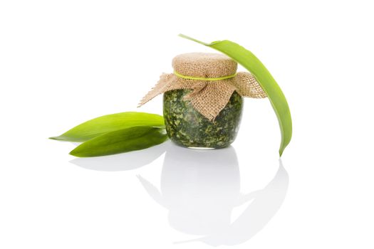 Garlic pesto in glass jar with fresh wild garlic leaves isolated on white background. Culinary healthy eating, spring detox. 