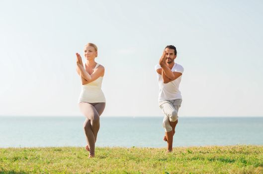 fitness, sport, friendship and lifestyle concept - smiling couple making yoga exercises outdoors