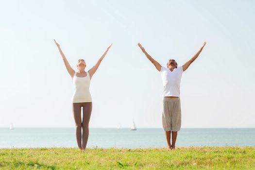 fitness, sport, friendship and lifestyle concept - smiling couple making yoga exercises outdoors