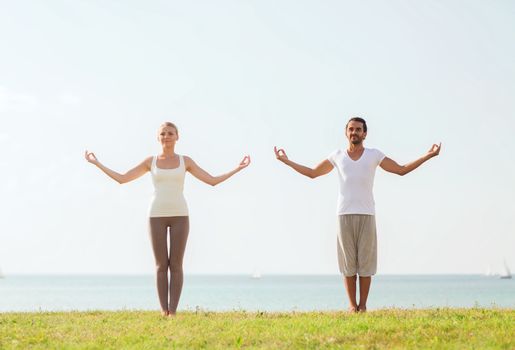 fitness, sport, friendship and lifestyle concept - smiling couple making yoga exercises outdoors