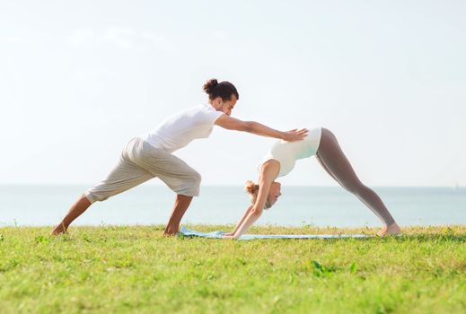 fitness, sport, friendship and lifestyle concept - smiling couple making yoga exercises on mat outdoors