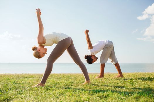 fitness, sport, friendship and lifestyle concept - smiling couple making yoga exercises outdoors