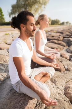 fitness, sport, friendship and lifestyle concept - smiling couple making yoga exercises sitting outdoors