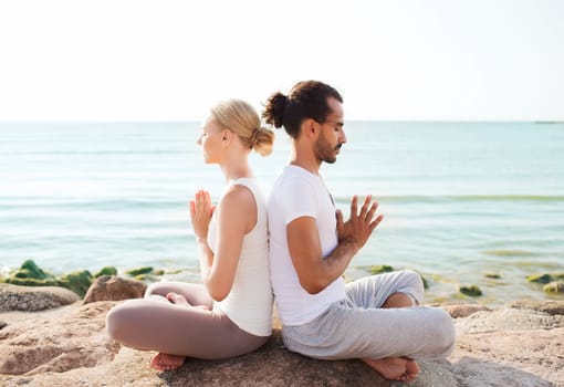 fitness, sport, friendship and lifestyle concept - smiling couple making yoga exercises sitting outdoors