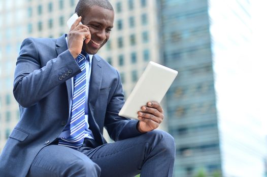 Businessman looking his tablet while talking on mobile